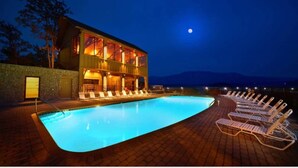 Una piscina con tumbonas, un edificio con grandes ventanales y un cielo nocturno con luna visible.