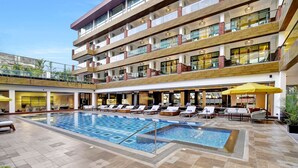 Hotel amb diverses plantes, piscina, zona d'estar a l'aire lliure i espai cobert amb ombrelles.