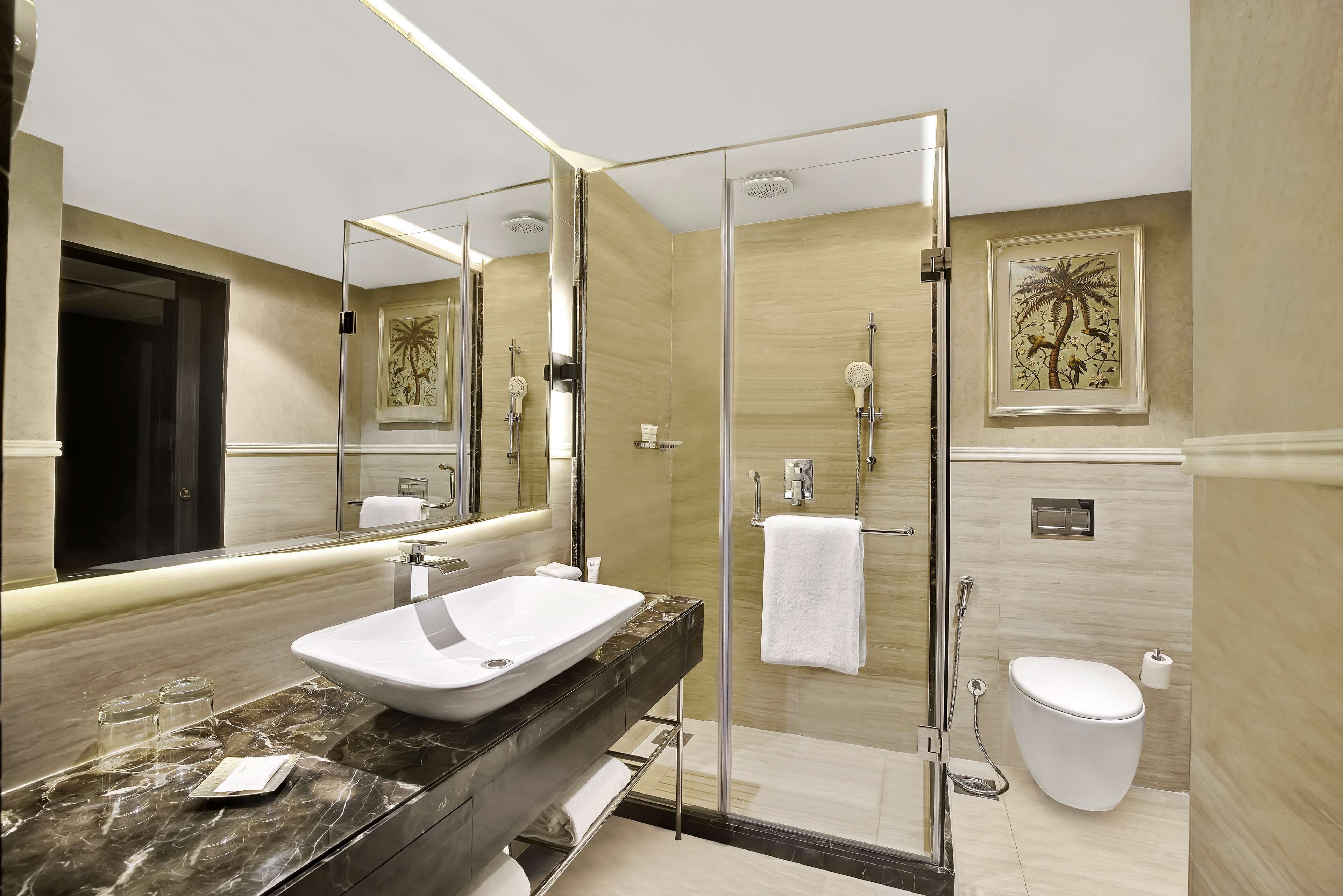 A modern bathroom with a large mirror, a white sink, a glass-enclosed shower, and a toilet.