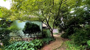 En brobelagt sti der fører til et hus omgivet af frodig vegetation og forskellige planter.