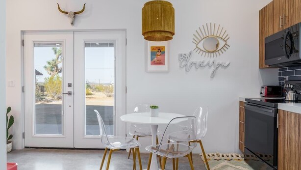 Een moderne keuken met een witte eettafel, transparante stoelen en een hanglamp.