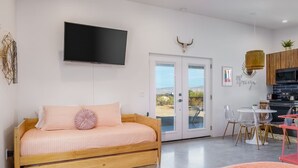 Een moderne slaapkamer met een houten bed, een aan de muur bevestigde televisie en een keuken die zichtbaar is door een open deur.