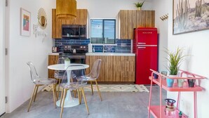 Een moderne keuken met een rode koelkast, houten keukenkastjes en een eethoek met transparante stoelen.