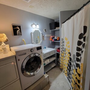 Een praktische badkamer met een wasmachine, een wastafel, een spiegel en een douchegordijn.