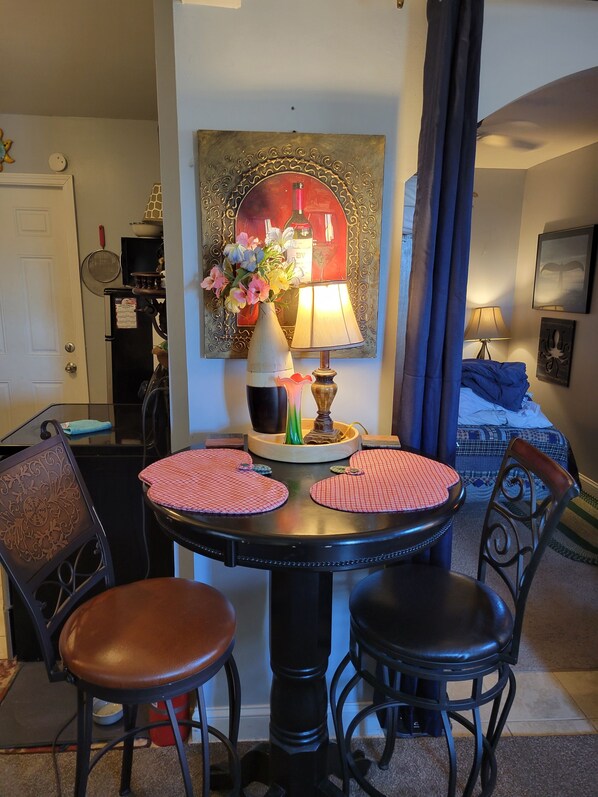 A dining area with a round table, two chairs, a vase of flowers, a lamp, and a painting on the wall.