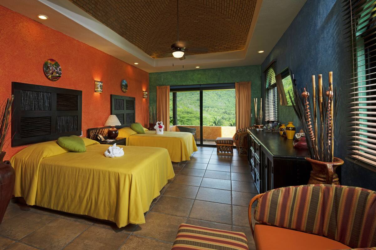 A hotel room with two beds, a sitting area, and a view of the outdoors.