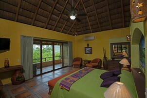 Una habitación con cama, dos sillas, una mesa, televisor y un ventanal grande.