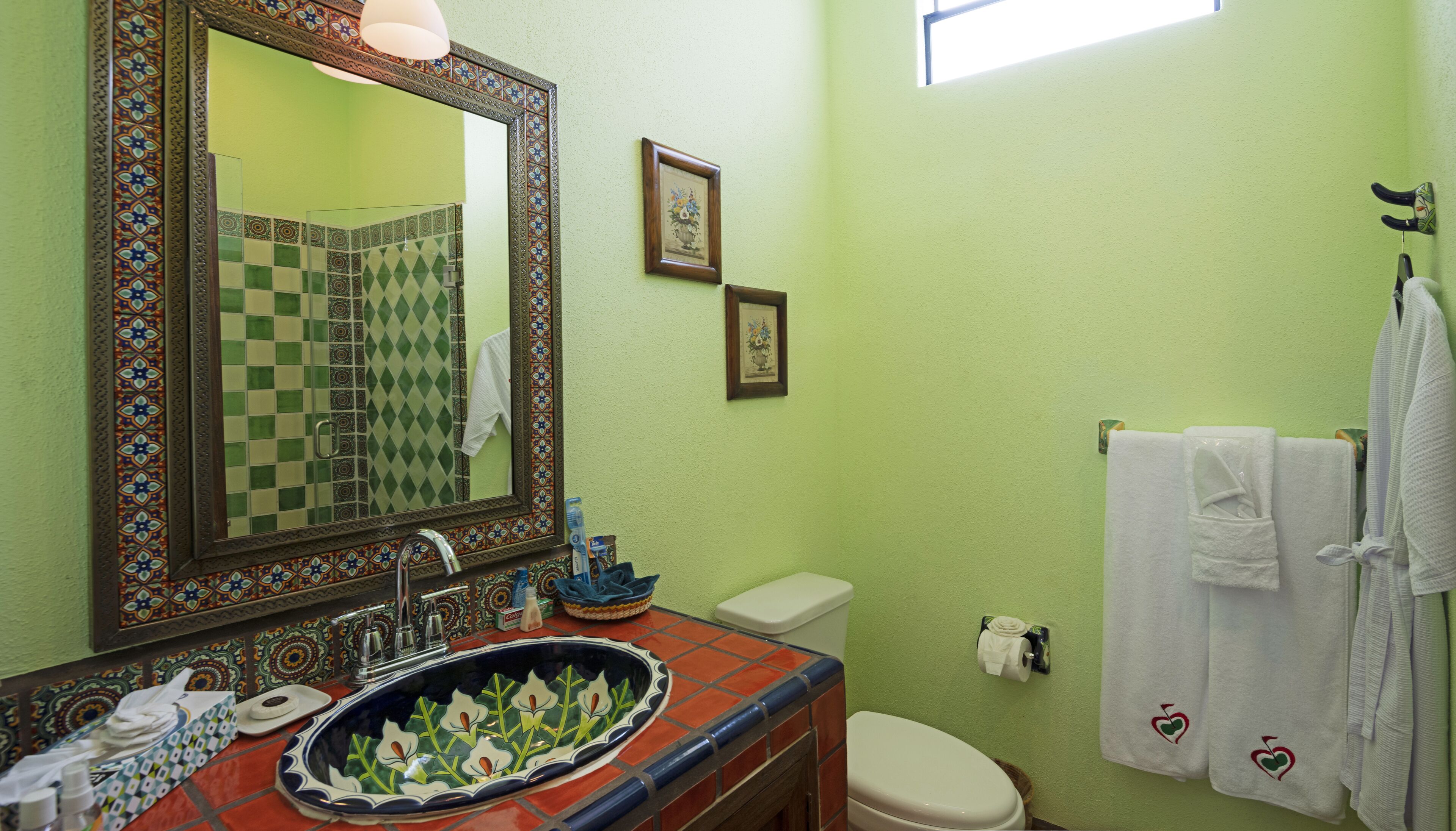 Un baño con un espejo grande, un lavabo con un cuenco decorativo, un inodoro y un perchero con toallas.
