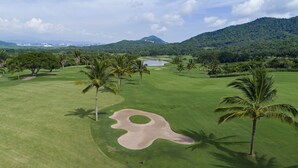 A golf course with a large sand bunker, palm trees, and a lake in the background. - El Corazón Golf & Spa Resort Manzanillo (Manzanillo)