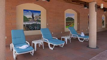 A covered outdoor seating area with white lounge chairs and a tiled floor.