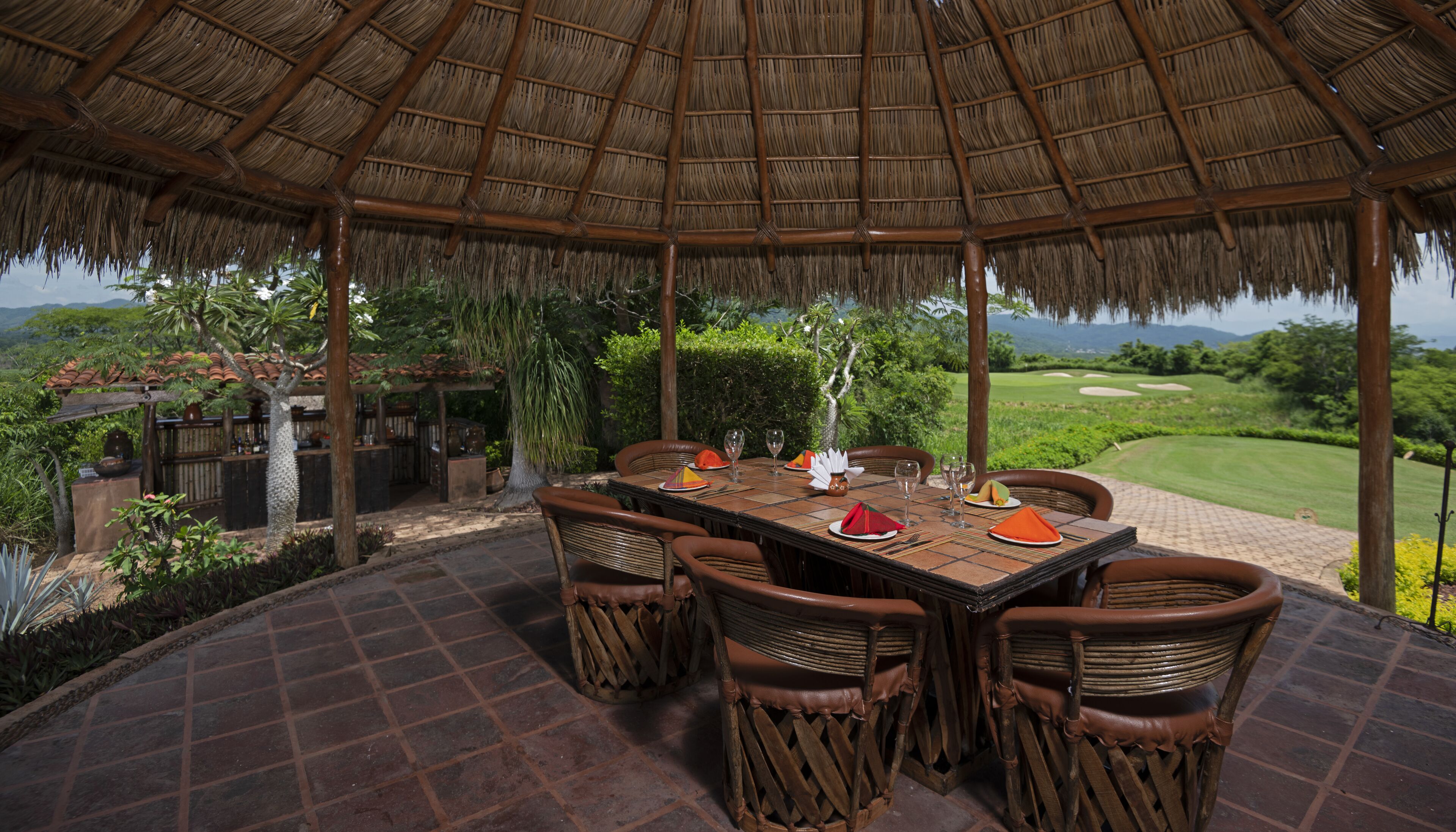 A covered outdoor dining area with a table set for four, surrounded by wicker chairs, overlooking a golf course.