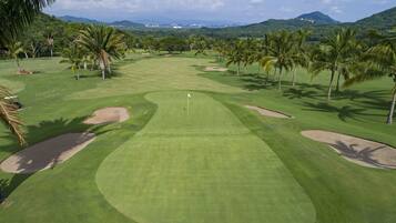 Campo de golf con un mástil de bandera, palmeras y búnkeres de arena.