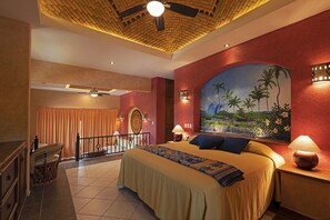A hotel room with a large bed, a ceiling fan, a painting of palm trees, and a balcony with a view. - El Corazón Golf & Spa Resort Manzanillo (Manzanillo)
