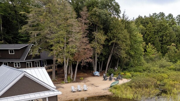 A lakeside cabin with a dock extending into the water, featuring outdoor seating and a covered area. - A Hidden Gem with Sandy Shore Memories and Island Views. (Township of Muskoka Lakes)