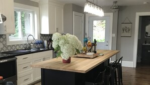 A modern kitchen with white cabinets, a wooden island, and a black dining table. - A Hidden Gem with Sandy Shore Memories and Island Views. (Township of Muskoka Lakes)