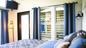 Ein Schlafzimmer mit einem Bett, einem an der Wand montierten Fernseher und einer Schiebeglastür, die auf einen Balkon führt.