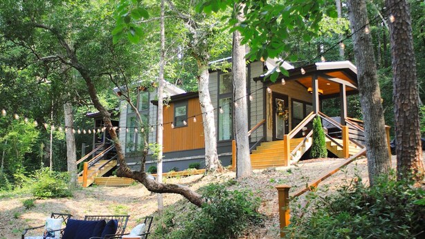 Eine Holzhütte mit einer Treppe, die zu einer Terrasse führt, umgeben von Bäumen.