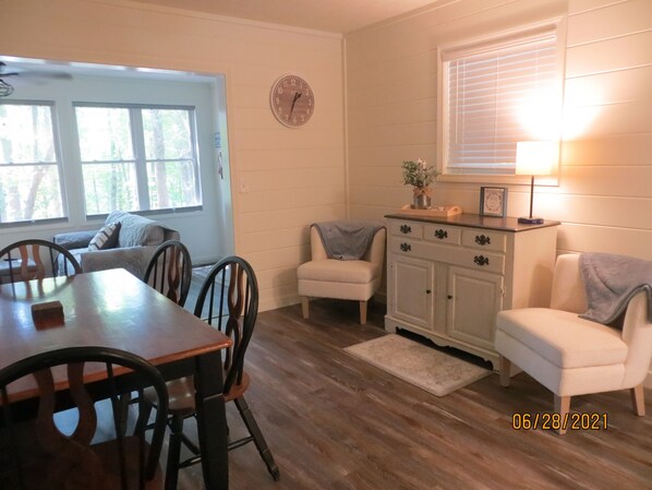 A dining area with a wooden table and chairs, a small cabinet with a clock, and a window with blinds. - LAKEFRONT Retreat! <br>Escape To Lake Hartwell in this lakeside cottage! (Lavonia)