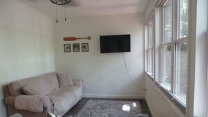 A living room with a beige sofa, a flat-screen TV mounted on the wall, and a wooden paddle on the wall above the TV. - LAKEFRONT Retreat! <br>Escape To Lake Hartwell in this lakeside cottage!  (Lavonia)