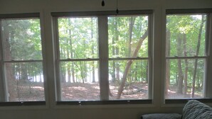 A room with three large windows offering a view of a forested area. - LAKEFRONT Retreat! <br>Escape To Lake Hartwell in this lakeside cottage!  (Lavonia)