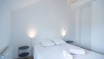 Une chambre moderne avec un grand lit, deux tables de chevet, un radiateur et une suspension au design géométrique original.