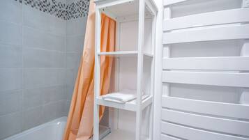 Ein Badezimmer mit einer weißen Badewanne, einer Duschvorhang und einem weißen Regal.