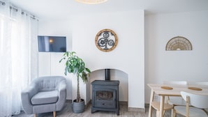 A modern living room with a grey armchair, a wooden table with chairs, a fireplace, a wall-mounted clock, and a large potted plant. - Le Duplex du Lac d'Orient #3 - Near the lake (Mesnil-Saint-Père)