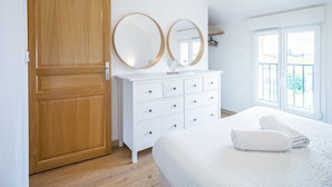 A bedroom with a wooden door, a white dresser with drawers, two round mirrors, a bed with a white blanket, and a hanging light fixture. - Le Duplex du Lac d'Orient #3 - Near the lake (Mesnil-Saint-Père)