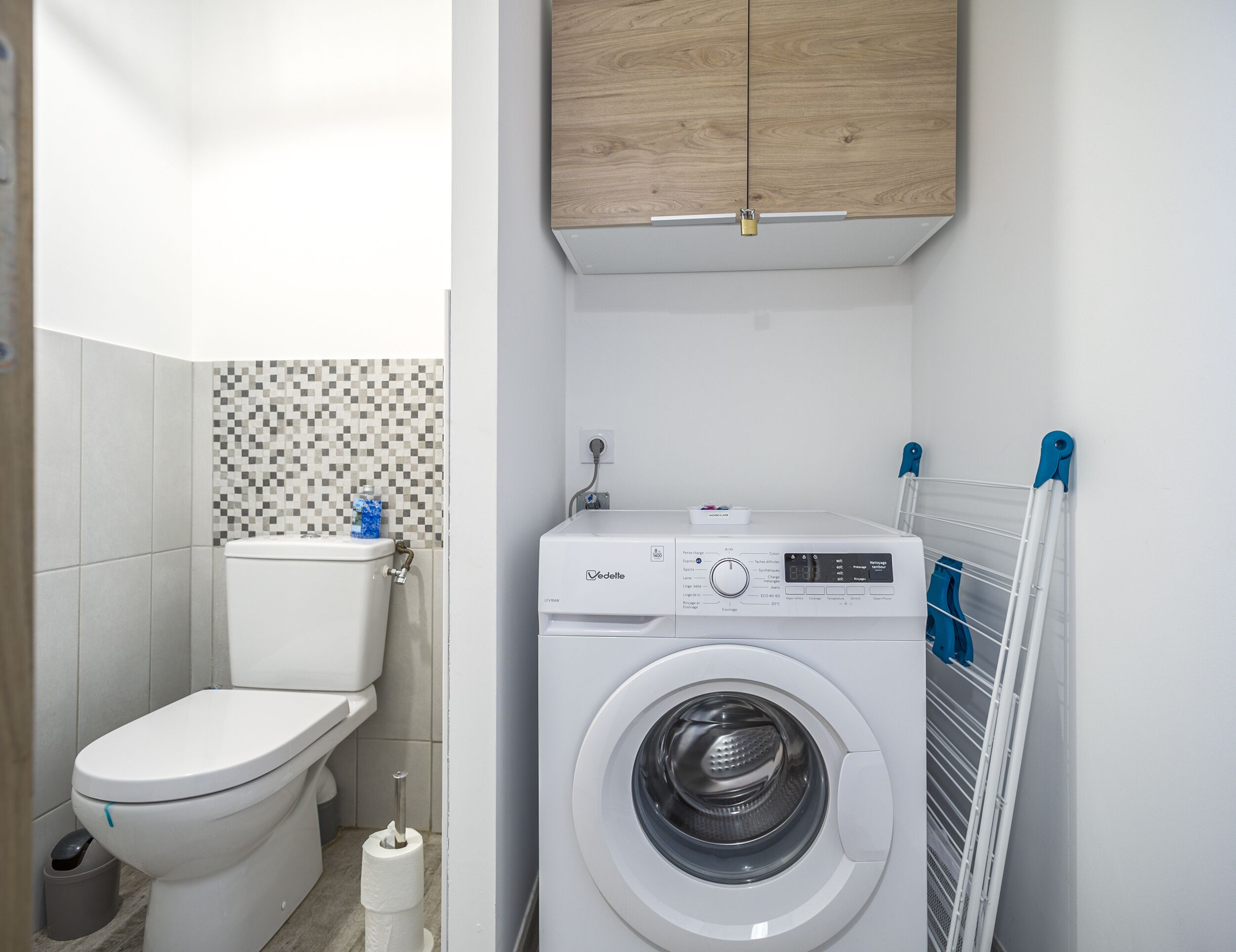 Un baño pequeño con inodoro, lavadora y pared de azulejos.