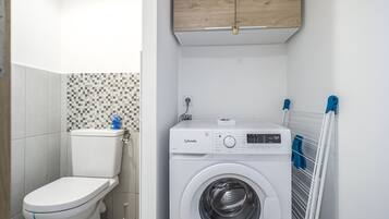 Un baño pequeño con inodoro, lavadora y pared de azulejos.