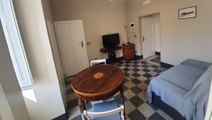 A room with a checkered floor, a wooden table with a chair, a bed, a TV, and a door. - Period house in the murattiano suburb- CIS: BA07203091000021052 (Monopoli)