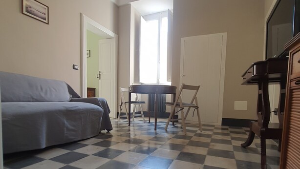 A room with a checkered floor, a sofa, a table, and chairs. There is a door leading to another room and a window allowing natural light. - Period house in the murattiano suburb- CIS: BA07203091000021052 (Monopoli)