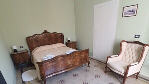A bedroom with a wooden bed, a chair, a chandelier, and patterned floor tiles. - Period house in the murattiano suburb- CIS: BA07203091000021052 (Monopoli)