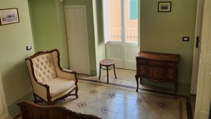 A room with a tufted armchair, a small round table, a wooden cabinet, a chandelier, and a door leading to a balcony. - Period house in the murattiano suburb- CIS: BA07203091000021052 (Monopoli)