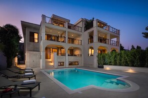 Un hôtel à plusieurs étages doté d’une piscine, de balcons et d’une façade bien éclairée.