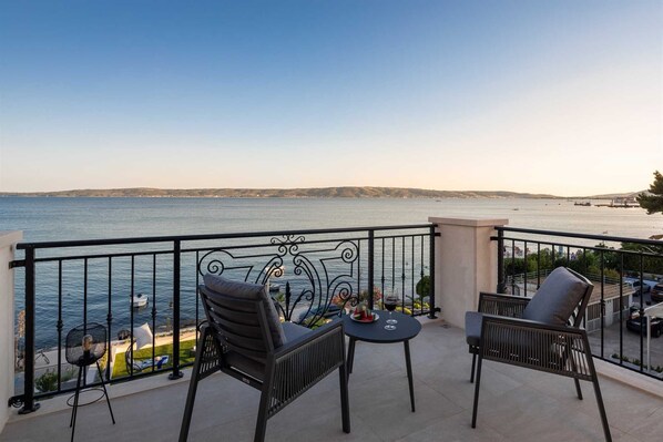 Un balcon avec deux chaises et une table, donnant sur une étendue d’eau et sur une terre lointaine.