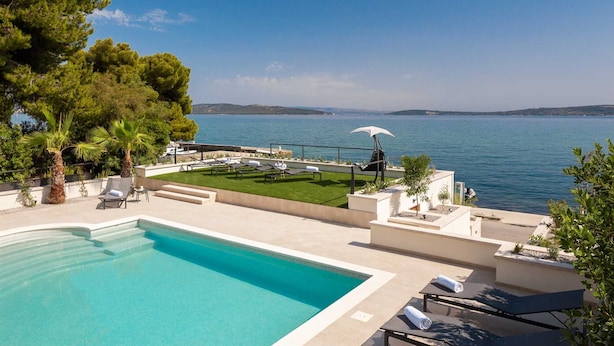A pool area with a view of the sea, lounge chairs, and a small garden. - Beachfront Villa Armeria with Pool (Kaštel Stari)