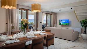 A modern hotel room with a dining area, a sofa, a TV, and a balcony with a scenic view. - Beachfront Villa Armeria with Pool (Kaštel Stari)