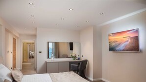 A hotel room with a bed, a desk with a mirror, a chair, and a painting of a sunset on the wall. - Beachfront Villa Armeria with Pool (Kaštel Stari)