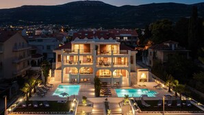 A multi-story hotel with a pool area, outdoor seating, and a view of the surrounding town and mountains. - Beachfront Villa Armeria with Pool (Kaštel Stari)
