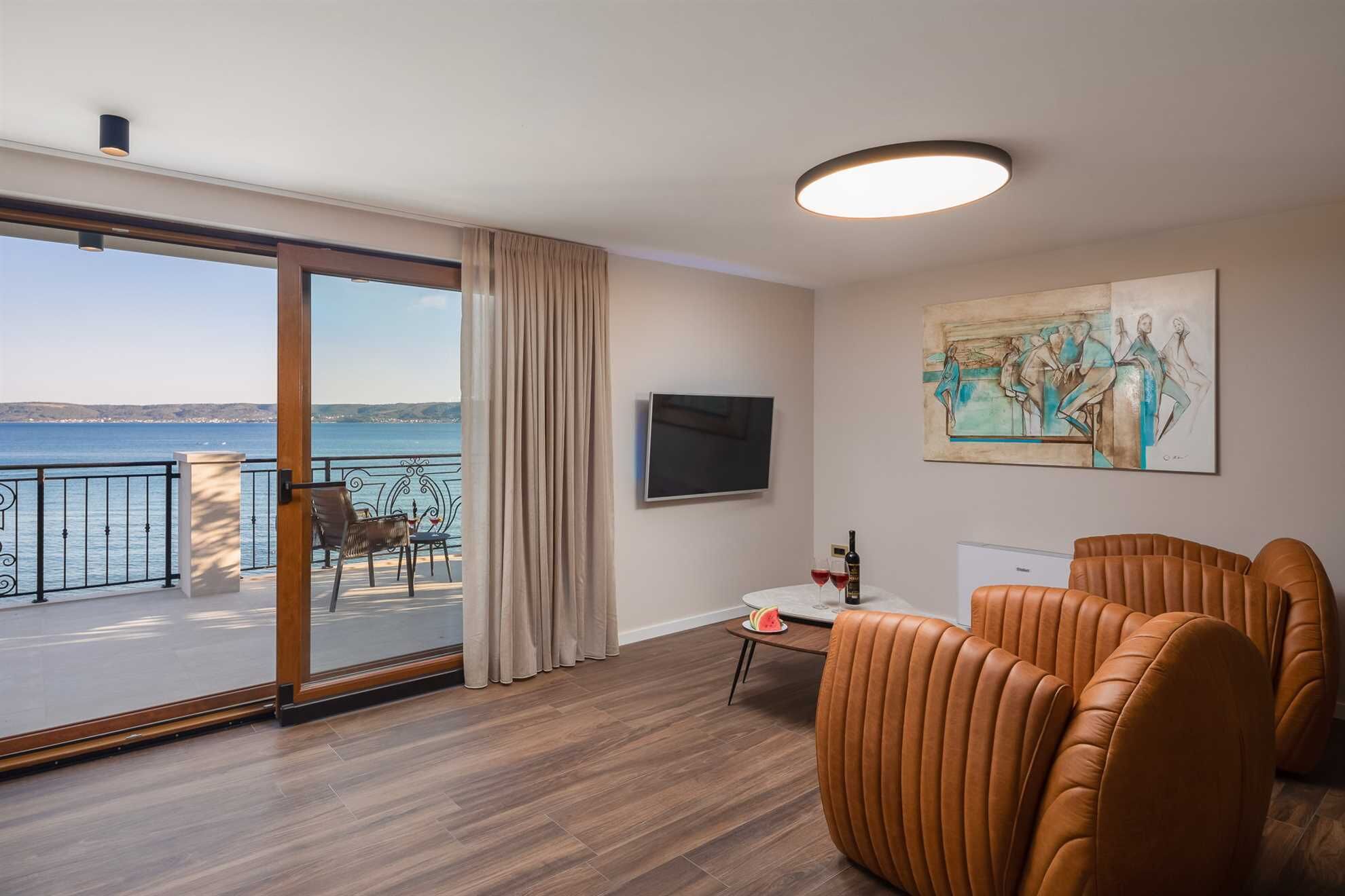 Habitació d'hotel moderna amb balcó, terres de fusta, televisió de pantalla plana, un quadre i butaques de pell.