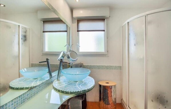 A bathroom with two round glass sinks, a mirror, and a small stool.