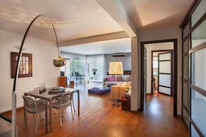 A spacious living area with a dining table, chairs, a sofa, and a lamp.