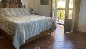 A bedroom with a bed, a nightstand, a lamp, a painting, and a view through an open door. - Honeymoon suite with private jacuzzi DISCOUNTED RATE (Loreto)