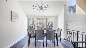 Un coin repas agrémenté d’un lustre, d’une table dressée pour quatre personnes et offrant une vue sur l’extérieur grâce à de grandes fenêtres.