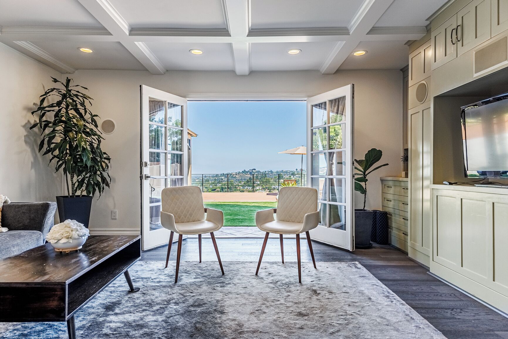 A modern kitchen with a large TV, open doors leading to a patio with a view of a baseball field.
