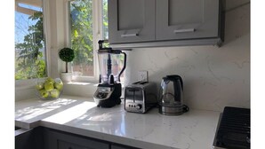 A kitchen with a blender, toaster, and coffee maker on the counter, a bowl of fruit, and a small plant.