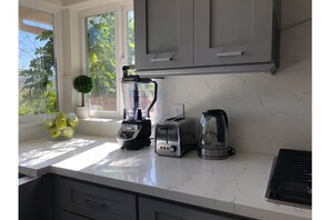 A kitchen with a blender, toaster, and coffee maker on the counter, a bowl of fruit, and a small plant.