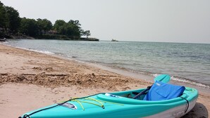 A kayak on a sandy beach with calm water and a distant shoreline. - UPPER 3 rm.  studio B&B steps from beach & farm markt/shop'g.; dogs ok w/fee.  (Port Austin)