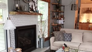 A cozy living room with a fireplace, a sofa, a coffee table, and a bookshelf. - UPPER 3 rm.  studio B&B steps from beach & farm markt/shop'g.; dogs ok w/fee.  (Port Austin)